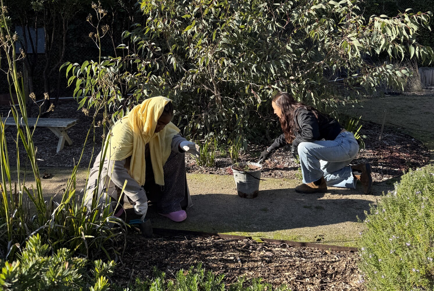 Two women gardening with trowels in a garden bed.
